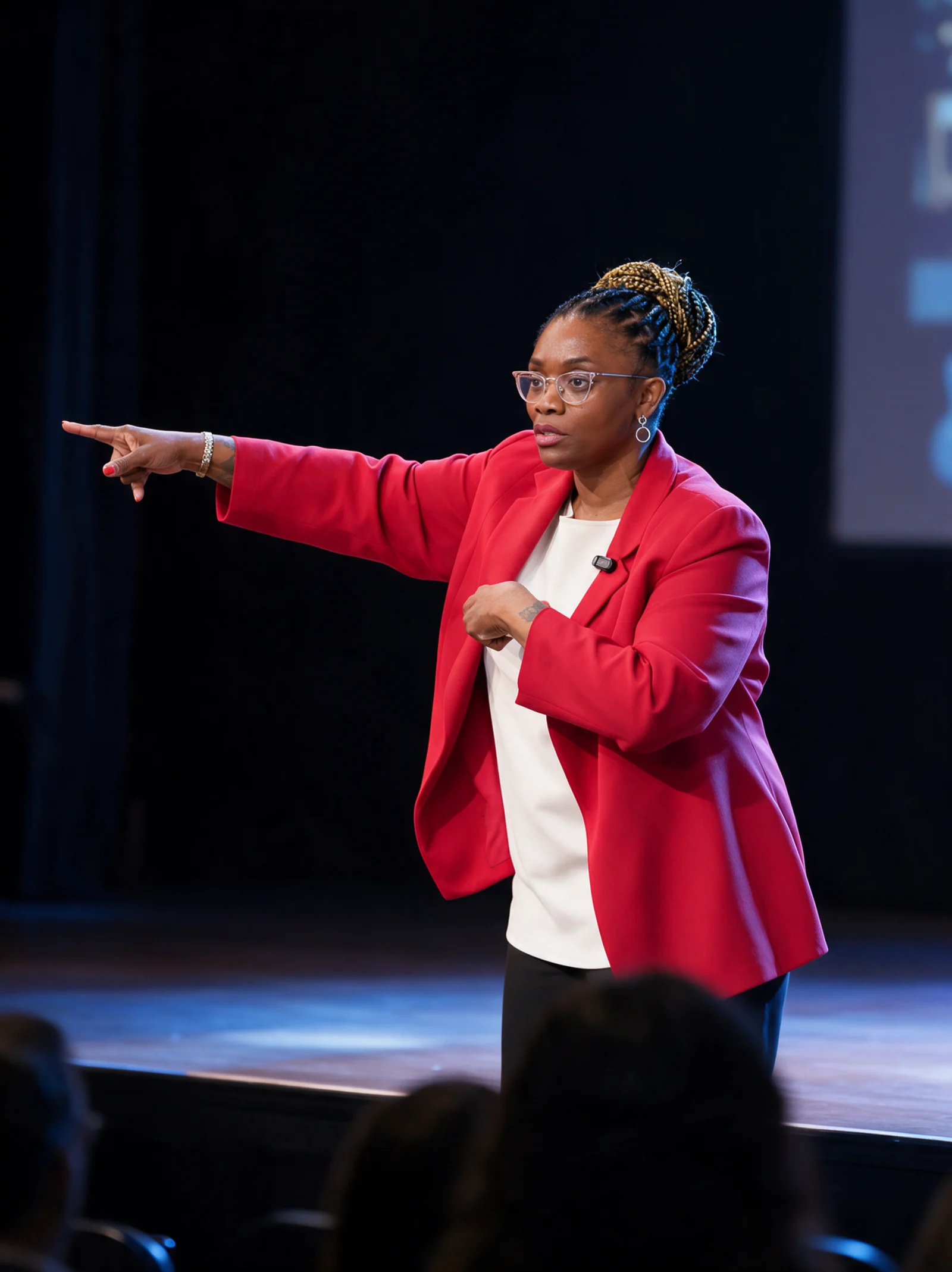 Dorothy Botsoe speaking on stage in a red blazer, pointing toward a screen while addressing an audience